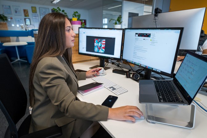 AI Act - Kennzeichung für AI generierte Inhalte. Frau sitzt vor mehreren Bildschirmen und erledigt kreative Arbeit