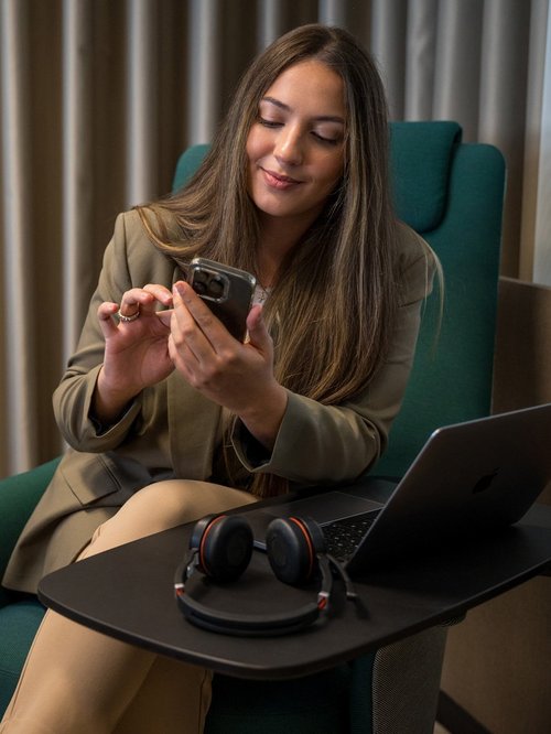 SIWA Marketing Mitarbeiterin mit Smartphone in der Hand und Laptop neben ihr am Tisch