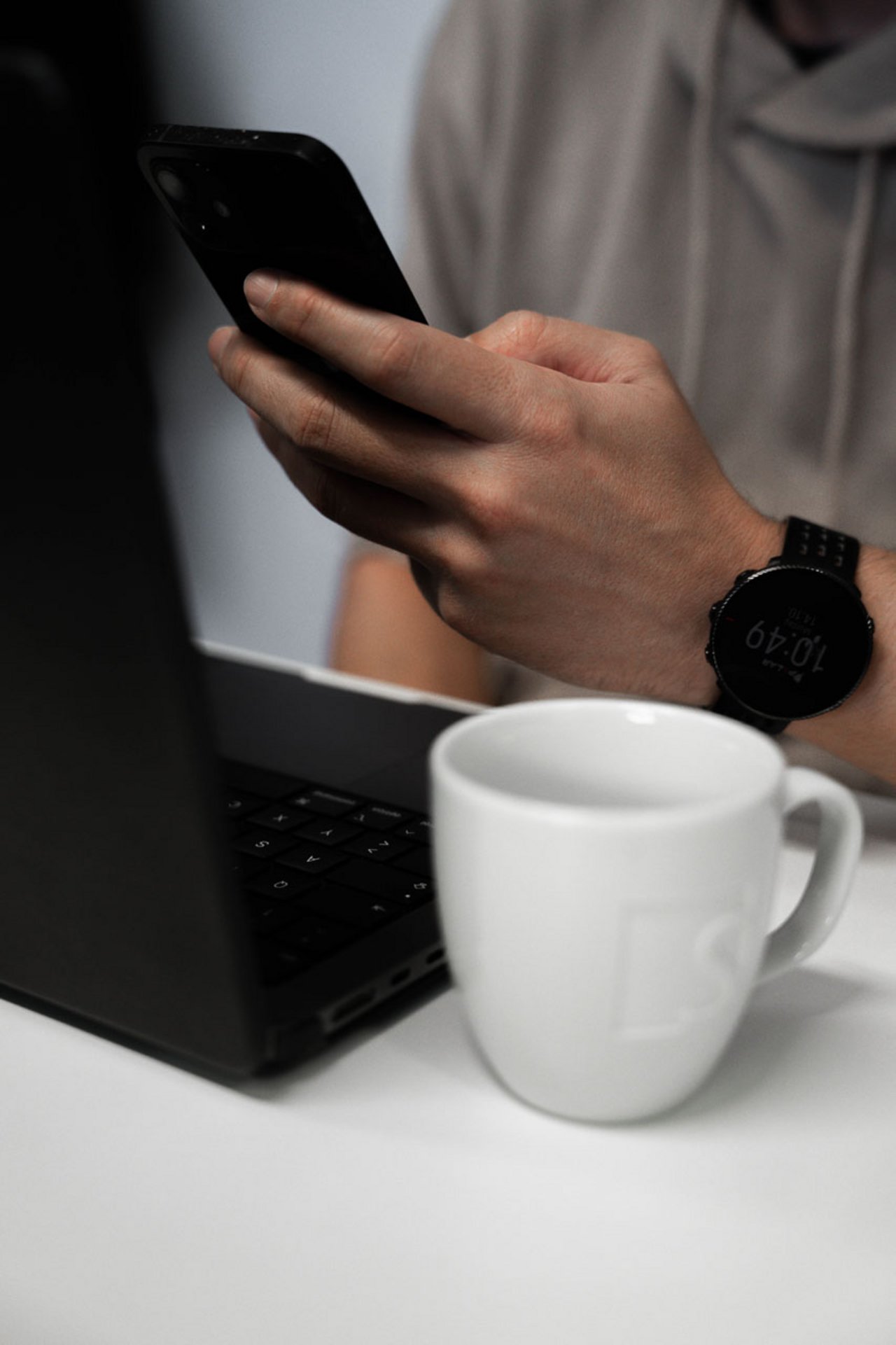 Imagebild mit Person die Smartphone bedient und vor einem Laptop sitzt. Daneben steht eine SIWA Kaffee Tasse